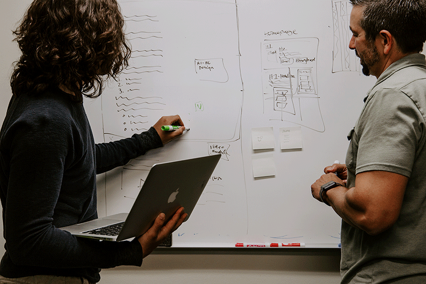 Two people discussing in front of a white board