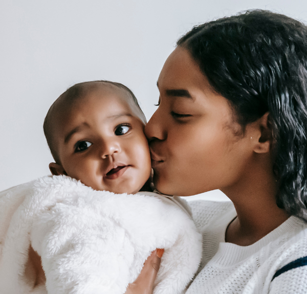 Mother holding her baby and giving it a kiss on the cheek.